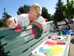 Carol garrison paints flowers on a village bench. On Tuesday the artists were working on the benches in Goodrich.  Photo by Patrick McAbee. 